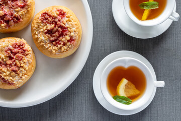 Sweet donuts on plates and small cups with mint tea on grey table. Tasty breakfast. Top view