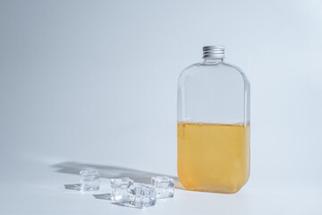 drink in a glass bottle on white background with hard or Harsh shadows and sunlight of leaves tree branch falling on wall. modern and minimal product design. cold refreshment beverage.