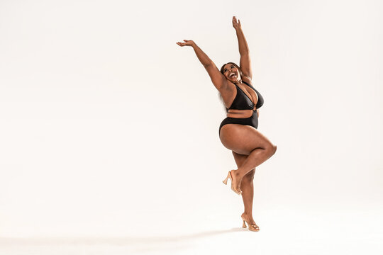 Full photo of happy, wonderful plus size African girl wearing black fashionable swimsuit, laughing and dancing.Concept of body acceptance, body positivity