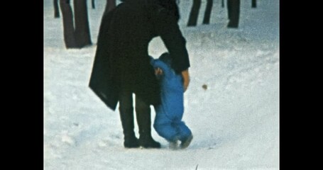 Funny little child falls on slippery snow in winter, mother helps to get up. Small kid in blue jacket walks with mother in snowy park. Happy family. Vintage color film. Family archive. Retro 1980s