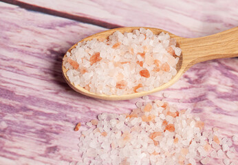 Large crystals pink Himalayan salt in wooden spoon on wood background.Top view