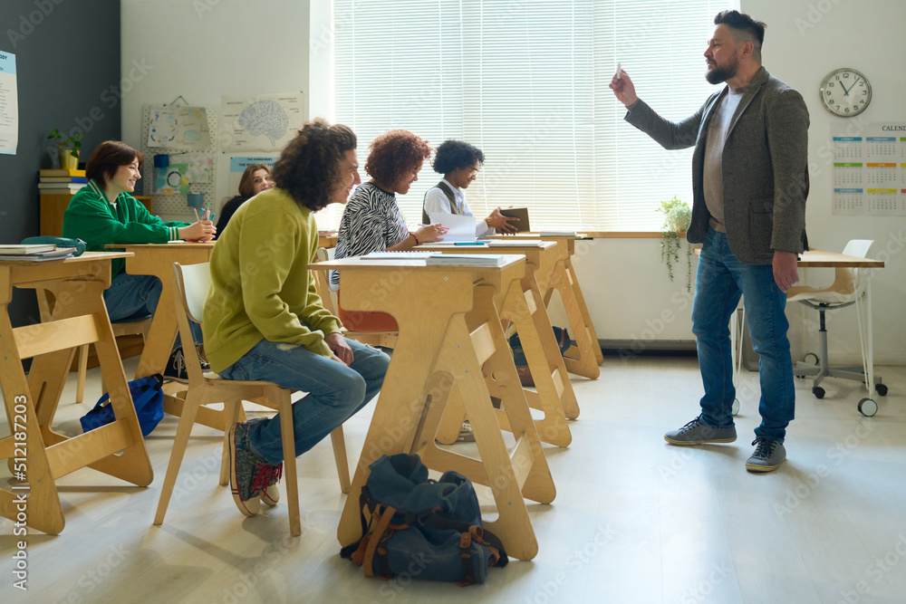 Poster group of students sitting by desks in classroom and listening to explanation of teacher standing in 