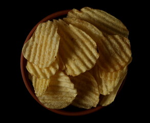 Potato chips, crisps in clay pot isolated on black, top view
