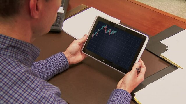 A business man sitting at his desk checks the weekly stock market wick and candle chart on a tablet PC. Graph shows a down bear market.  	