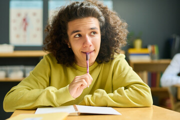 Clever teenage guy in casualwear looking at teacher explaining new subject by blackboard or...