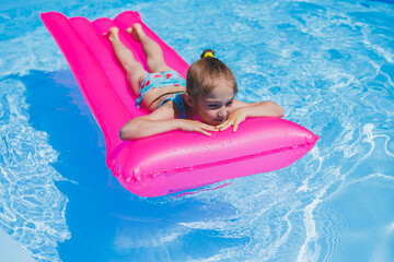 Girl 7-8 years old swims in the pool on an inflatable pink mattress. Summer holidays