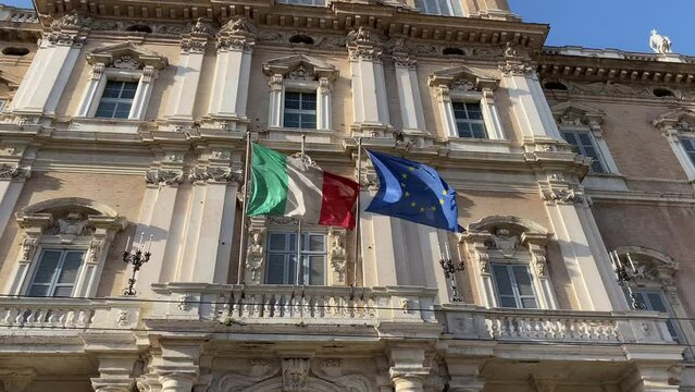Italian and European flags waving in the wind of the facade of goverment palace