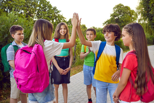 Group of school children having fun in the park. Cheerful little friends playing games outdoors. Happy boy and girl standing on a park path and giving each other a high five. Teamwork and fun concept