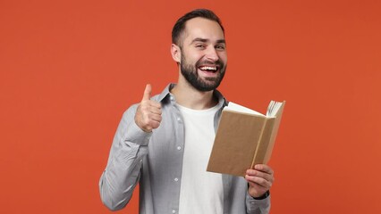 Smiling fancy amazing swanky young brunet man 20s years old wear blue shirt reading book isolated on plain orange background studio portrait. Education high school collage university free time concept - Powered by Adobe