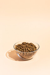 Dry food in a transparent bowl for cats and dogs on a beige, peach background