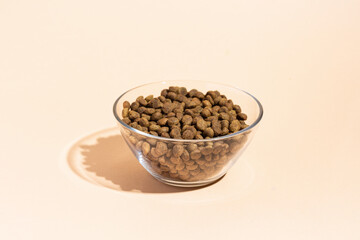 Dry food in a transparent bowl for cats and dogs on a beige, peach background