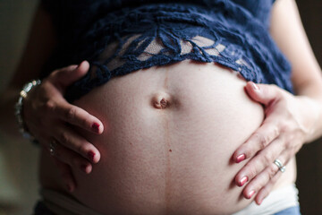 A woman holds her hands on her pregnant belly. - obrazy, fototapety, plakaty
