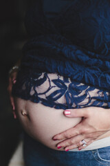 A woman holds her hands on her pregnant belly.