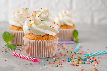 Delicious vanilla cupcakes with cream cheese and sugar candy on a gray background. Dessert for birthday. selective focus, copy space.