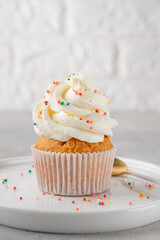 Delicious vanilla cupcakes with cream cheese and sugar candy on a gray background. Dessert for...