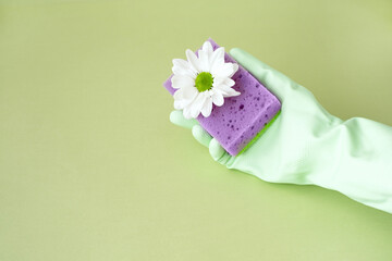 Hand in green rubber glove holding a dishwashing sponge on green background for design with copy space. Concept soft and reliable protection of the skin of the hands, washing dishes, cleaning..