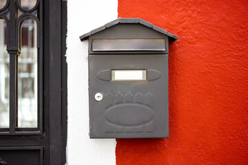 Metal grey mailbox, postbox on red and white wall. A box for letters, correspondence delivered to a...