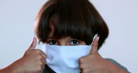 Child wearing surgical mask giving thumbs up, kid portrait wearing pandemic mask