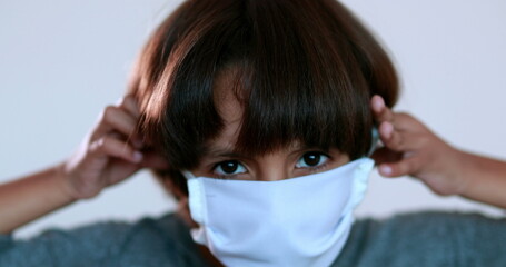 Child putting on covid-19 mask against pandemic prevention. Mixed race kid wearing surgical mask giving thumps up