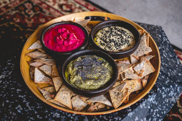 Round wooden tray with delicious and colorful vegetarian/vegan catering with three types of vegan hummus (natural, olive and beetroot) and baked salty toasts