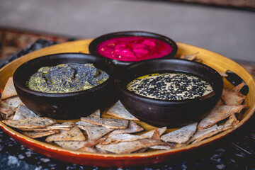 Round wooden tray with delicious and colorful vegetarian/vegan catering with three types of vegan hummus (natural, olive and beetroot) and baked salty toasts