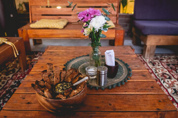 Wooden table with delicious vegetarian/vegan catering with hummus with black sesame and baked salty toasts with olive and flowers decoration