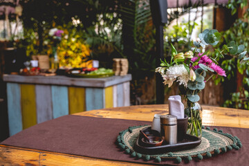 Wooden table with bottle with flowers decoration in water, dressings and colorful vegan catering in a table in the background in a garden wedding party