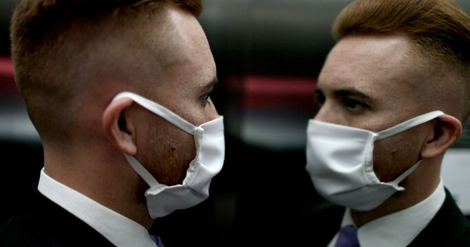 Business man commuting wearing covid-19 mask inside elevator, person looking at mirror wearing pandemic mask