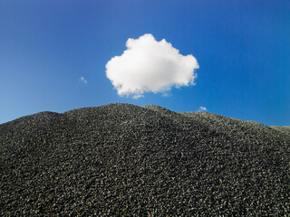 Pile of small stones against blue sky and lone white cloud in blue sky