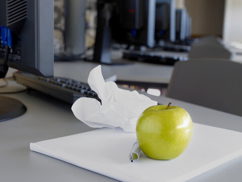 Green apple and pen resting on pad next to computer 