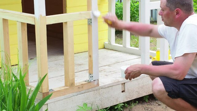 a man paints the terrace with a brush with white paint. dad makes a children's house or hut for his daughter