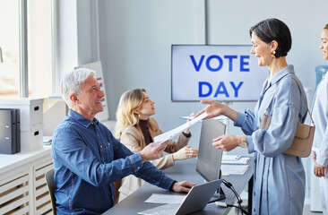 Obraz premium Side view portrait of smiling adult woman taking ballot form while voting on election day, copy space