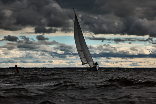 Sailboat in sea at stormy weather, stormy clouds sky orange sky, sail regatta, reflection of sail in the water, bigl waves of water, 