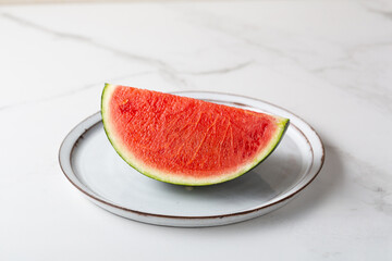 Slice of red watermelon on a plate on light surface