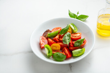 Close up of tomato summer salad in white bowl basil