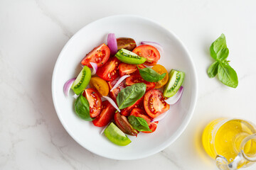 Top view of tomato summer salad in white bowl basil