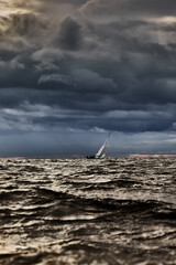 Sailboat in sea at stormy weather, blurred background, stormy clouds sky, sail regatta, reflection of sail in the water, big waves of water
