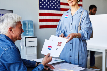 Close up of senior man handing out ballots and Voter stickers on election day, copy space