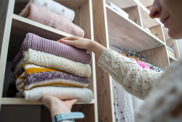 Woman choosing outfit from large wardrobe closet with stylish clothes and home stuff