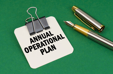 On a green surface, a pen and a sheet of paper with the inscription - Annual Operational Plan