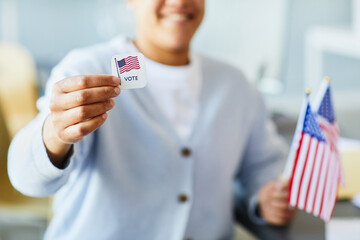 Close up of person holding voting sticker and American flag, focus on foreground, copy space