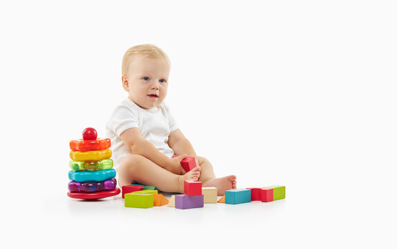 Cute baby plays with toys on a white isolated background. The child folds a constructor and a pyramid