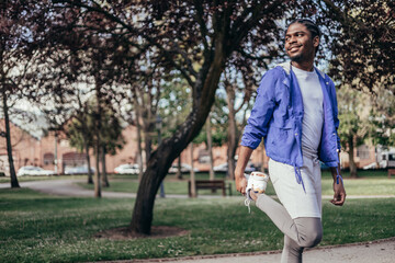 smiling african american young man stretching quadriceps in park