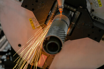 CNC laser cutting machine working with cylindrical metal workpiece with many sparks at factory,...