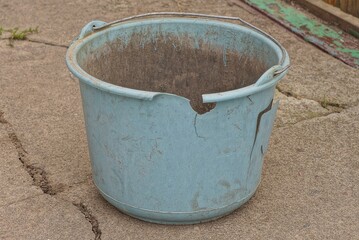 Fototapeta premium one old blue broken dirty plastic bucket with cracks stands on gray asphalt in the street 