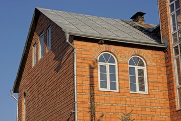 attic of a private red brick house with white windows under a gray slate roof outdoors against a blue sky