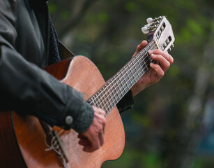 Hands of an adult man playing an acoustic guitar on the street, in a park close-up, selective...