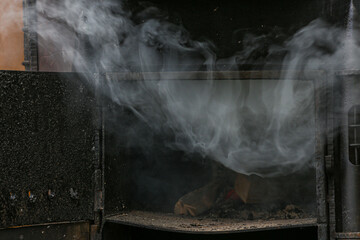 Thick smoke billows from a coal stove in close-up. Wood is burning in the oven.