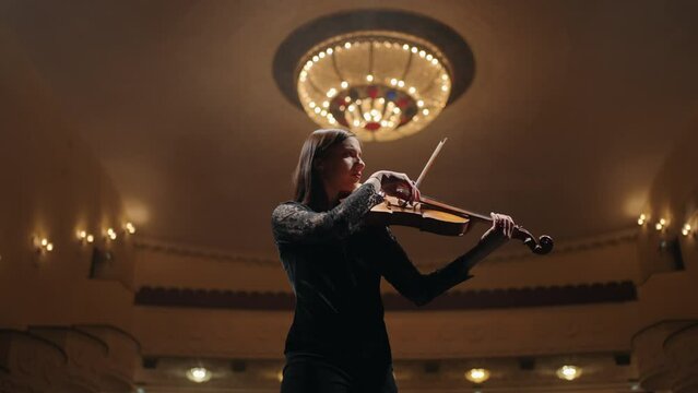 professional female violinist is playing violin on scene of opera house, portrait of soloist in philharmonic hall
