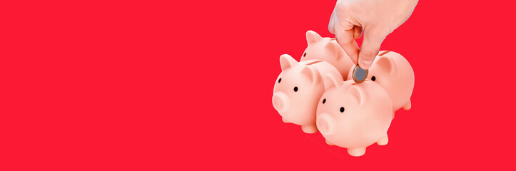 Hand putting coins to   piggi bank. Four pink piggy banks isolated on red  background